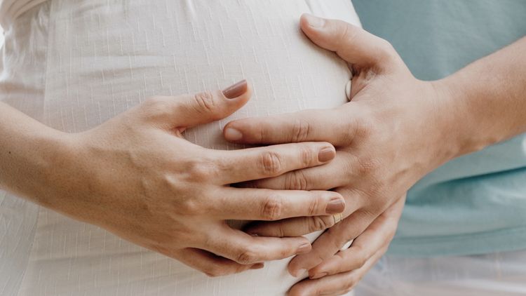 Femme enceinte se faisant toucher le
      ventre par un homme avec sa main reposant sur la sienne